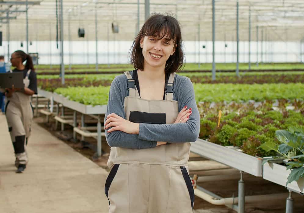 Bright-eyed woman in gardening apron inside greenhouses.